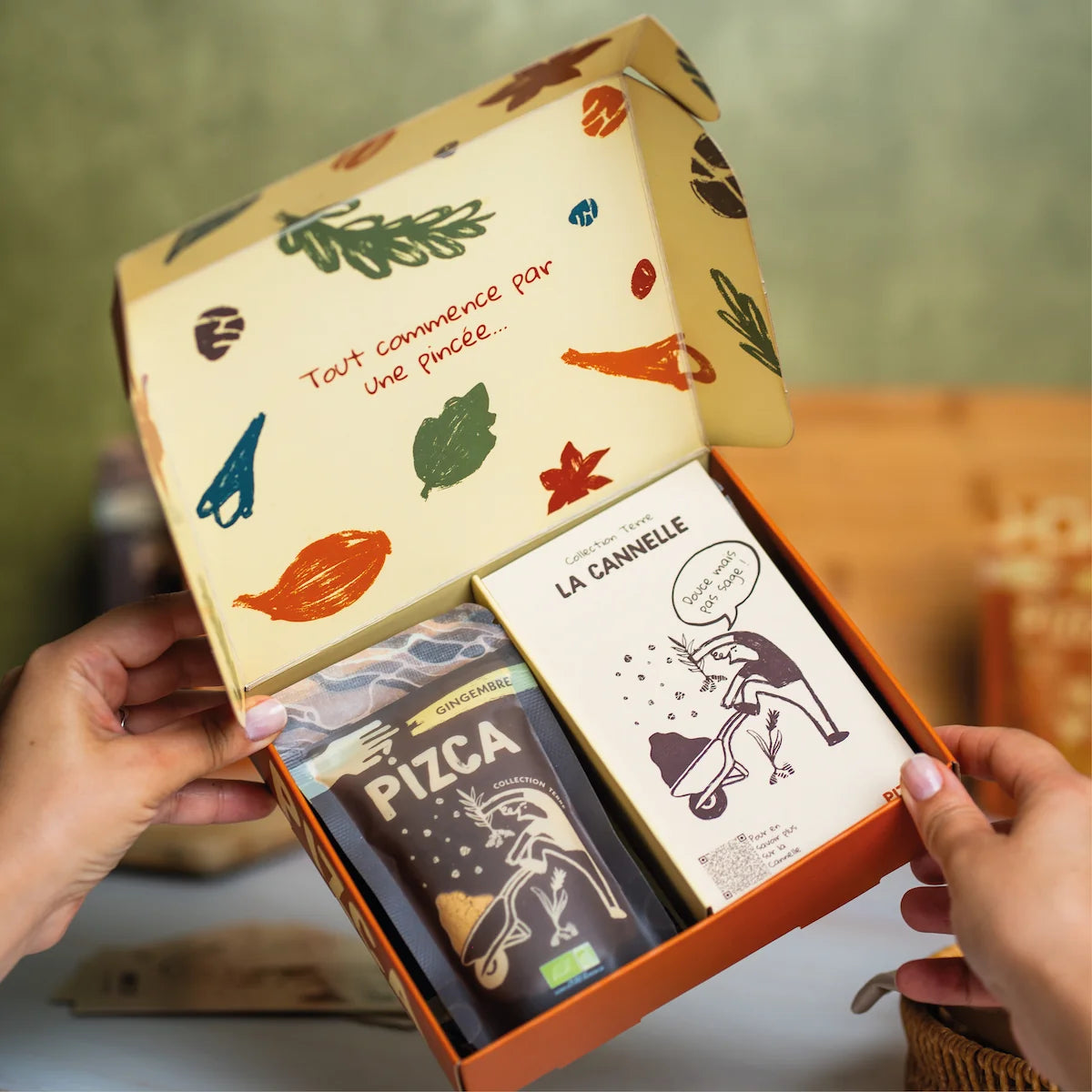 Coffret cadeau d'épices bio Pizca ouvert contenant un sachet de gingembre et une fiche recette de cannelle avec un design illustré moderne