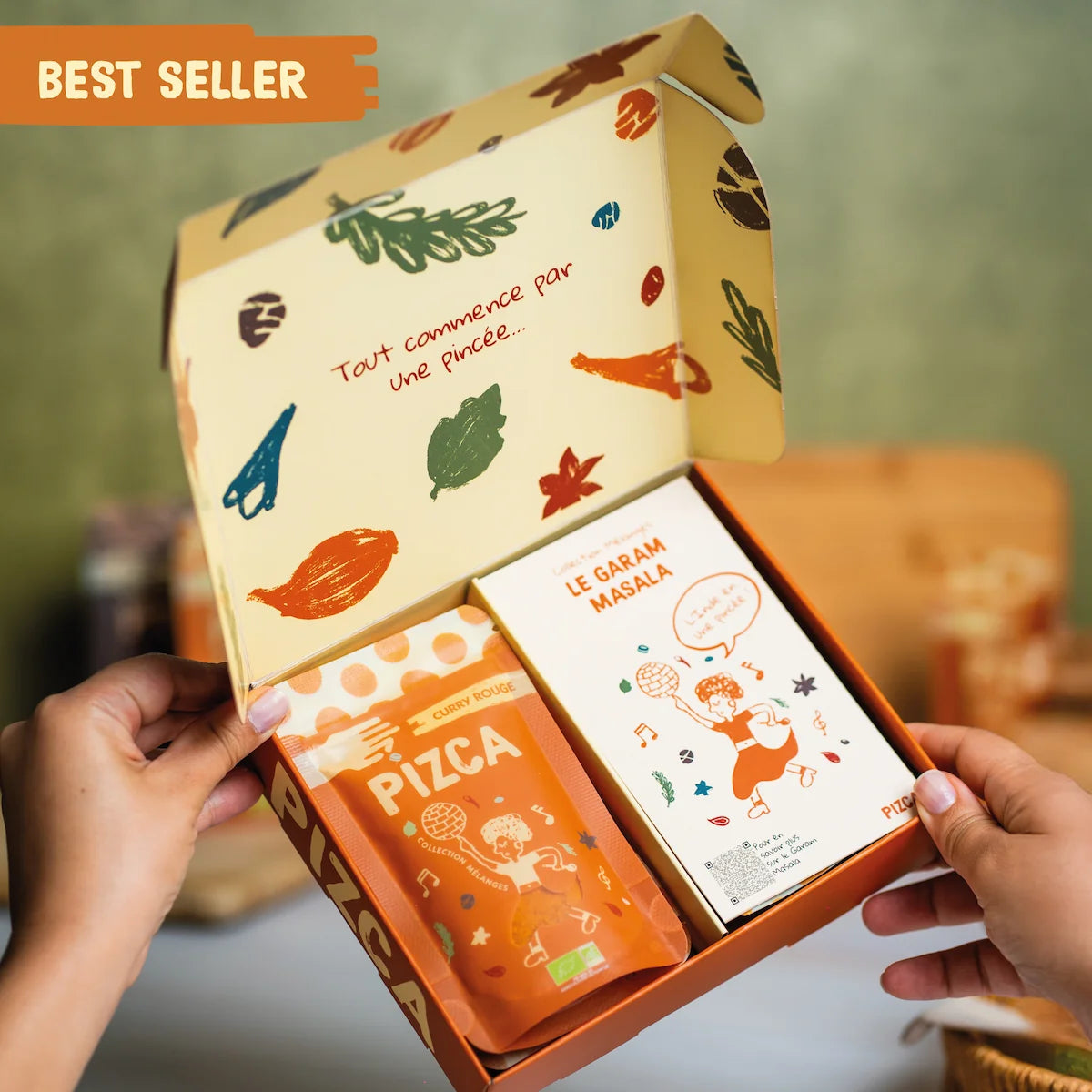 Coffret cadeau de mélanges d'épices bio Best Seller de la marque PIZCA ouvert contenant un sachet de curry rouge et une fiche recette de garam masala avec un design illustré moderne.